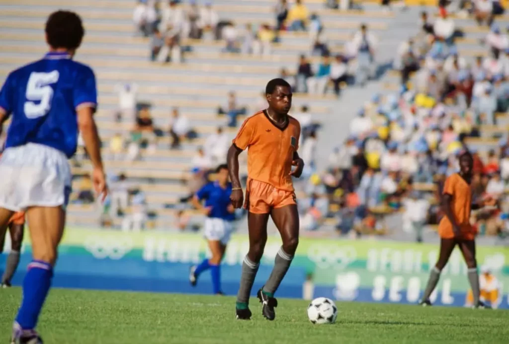 Kalusha Bwalya of Zambia (centre) on the pitch during the Zambia v Italy match during the 1988 Summer Olympics, Gwangju Mudeung Stadium, South Korea, 19th September 1988. Bwalya scored a hat-trick in the game and Zambia went on to beat Italy 4 - 0. (Photo by Bob Thomas Sports Photography via Getty Images)